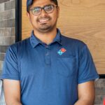 Raj Manchanda, CEO and founder of Domino’s Pizza Niagara Falls, standing inside his restaurant with pizza boxes and menu displays in the background.
