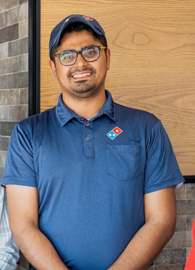 Raj Manchanda, CEO and founder of Domino’s Pizza Niagara Falls, standing inside his restaurant with pizza boxes and menu displays in the background.